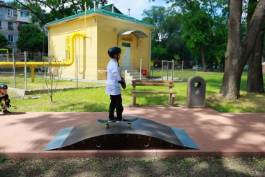 Beyaz çocuk kaykayla parkta koruyucu giysilerle geziyor. 31 Mayıs 2024 Balti Moldova.