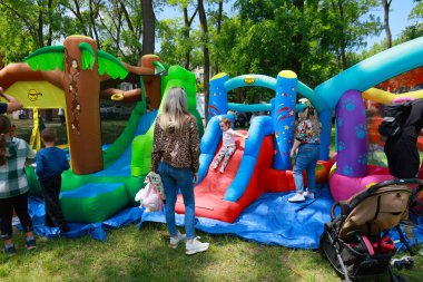 Çocuklar parktaki renkli şişme kaydırak üzerinde oynuyorlar ve yetişkinler izliyor. 31 Mayıs 2024 Balti Moldova.