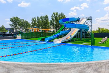 Slaytlı bir havuz ve yeşil ve mavi bir kaydırak. Havuz ağaçlarla çevrili ve yeşil bir çiti var. 8 Haziran 2024 Balti Moldova