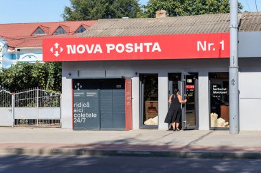 İspanyol kadın yetişkin, güneşli şehir ortamında Nova Poshta ofisine giriyor. 9 Eylül 2024 Balti Moldova.