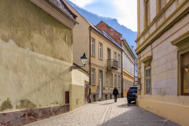 Dar bir sokak, bir sokak lambası ve yanına park edilmiş bir araba. Sokak binalarla dolu ve bir insan caddede yürüyor. 14 Aralık 2024 Brasov Romanya