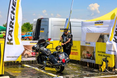 Bir motorcu, motosikletini dışarıdaki temizlik kabininde temizlemek için güçlü bir basınç makinası kullanır. Etkili araç temizleme ürünleri gösteriliyor. 2 Temmuz 2023 Liadoveni Moldova.