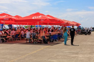 Ziyaretçiler parlak kırmızı şemsiyeler altında toplanarak, canlı bir açık havada gölgeli oturma ve günlük sohbetlerin keyfini çıkarıyorlar. 2 Temmuz 2023 Liadoveni Moldova.