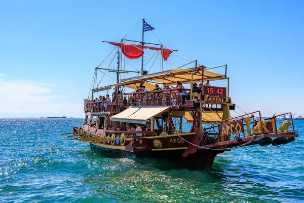 Kırmızı yelkenli ve beyaz tenteli büyük bir tekne okyanusta yüzüyor. Tekne insan kaynıyor ve teknede birkaç bayrak var. 8 Ağustos 2024 Selanik Yunanistan