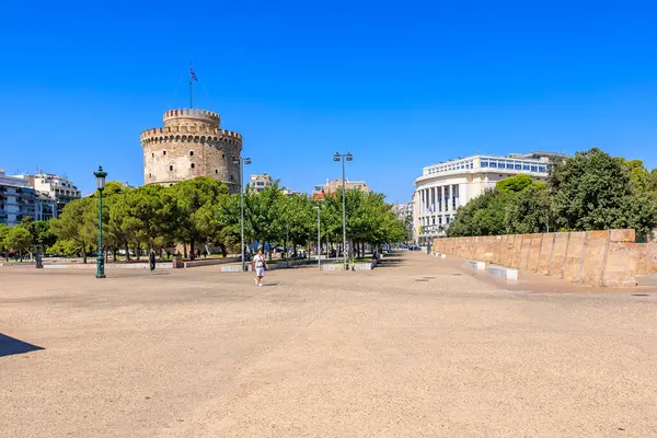 Arkasında büyük bir kule olan bir şehir meydanı. Gökyüzü açık ve mavi. Meydanın etrafında yürüyen birkaç kişi var. 8 Ağustos 2024 Selanik Yunanistan