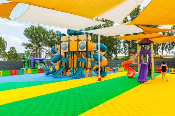 Sarı ve beyaz gölgelikli ve mavi ve turuncu slaytlı bir oyun alanı. Bir kadın oyun alanının yanından geçiyor. 8 Haziran 2024 Balti Moldova