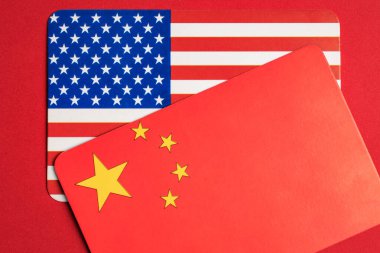 Kırmızı arka planda üst üste binen ABD ve Çin bayrakları gerginliği ve diplomasiyi simgeliyor.