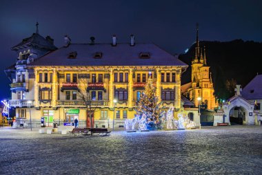 Bir binanın önünde bir Noel ağacı parlıyor. Sahne kasaba meydanında bir bank ve birkaç kişi ile çekiliyor. 13 Aralık 2024 Brasov Romanya
