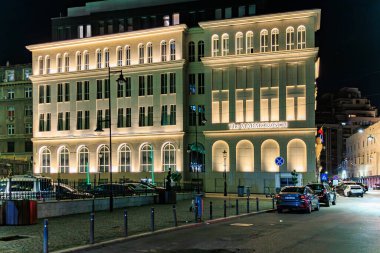 Aydınlanmış şehir binası ve caddelerde arabaları olan şık bir gece manzarası. 8 Mart 2025 Bükreş Romanya.