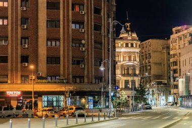 Aydınlatılmış tarihi binalar ve sokak aktiviteleriyle dolu kentsel gece manzaraları. 8 Mart 2025 Bükreş Romanya.