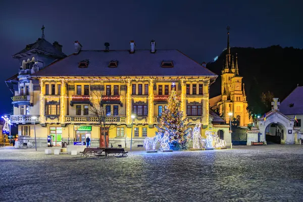 Bir binanın önünde bir Noel ağacı parlıyor. Sahne kasaba meydanında bir bank ve birkaç kişi ile çekiliyor. 13 Aralık 2024 Brasov Romanya