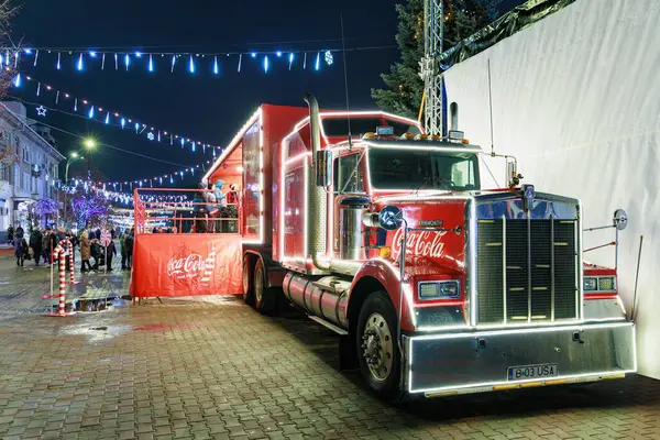 Şehir caddesinde gece vakti Noel ışıkları olan Coca-Cola kamyoneti sergisi. 27 Aralık 2024 Balti Moldova.