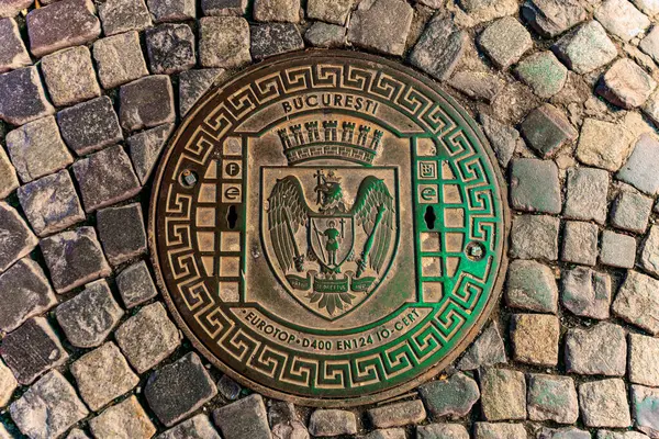 Şehir amblemi ve detaylı tasarımı olan kaldırım taşı caddesindeki Bükreş rögar kapağı. 8 Mart 2025 Bükreş Romanya.