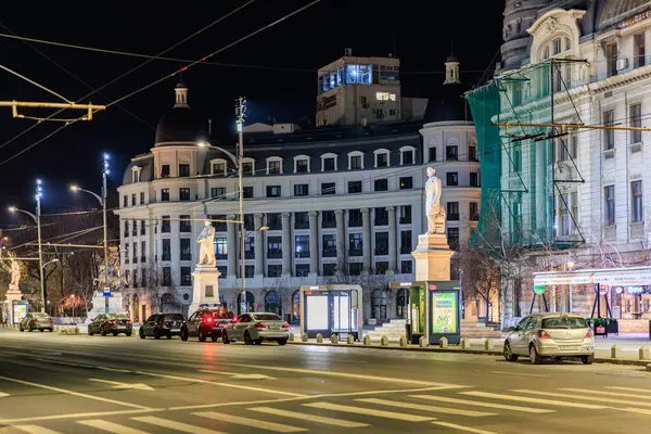 Heykelleri ve arabaları olan tarihi Avrupa şehir caddesinin gece manzarası. 8 Mart 2025 Bükreş Romanya.