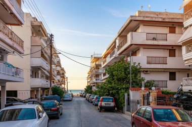 Üzerinde bir sürü araba olan bir cadde. Arabaların çoğu beyaz ve kırmızı. Sokak binalarla dolu ve arka planda bir plaj var. 8 Ağustos 2024 Perea Yunanistan