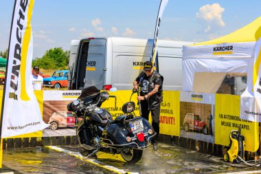 Bir motorcu, motosikletini dışarıdaki temizlik kabininde temizlemek için güçlü bir basınç makinası kullanır. Etkili araç temizleme ürünleri gösteriliyor. 2 Temmuz 2023 Liadoveni Moldova.