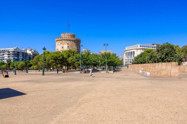 Arkasında büyük bir kule olan bir şehir meydanı. Gökyüzü açık ve mavi. Meydanın etrafında yürüyen birkaç kişi var. 8 Ağustos 2024 Selanik Yunanistan
