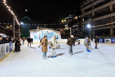 Farklı insanların kış eğlencesinin tadını çıkardığı gece buz pateni pisti. 27 Aralık 2024 Balti Moldova.