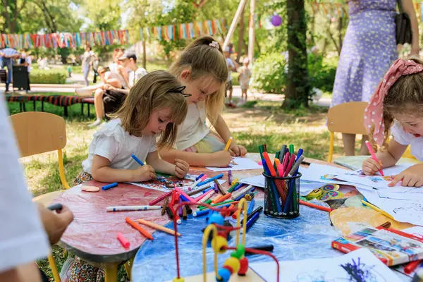 Üç küçük kız bir masada bir sürü boya kalemi ve boyama kitabıyla oturuyorlar. Birlikte resim çizip boyuyorlar. 1 Haziran 2024 Balti Moldova.