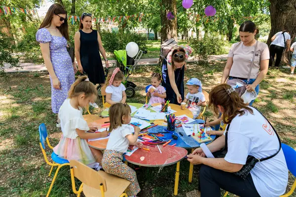 Bir grup çocuk bir masanın etrafında oturuyorlar. Masanın yanında bir kadın yerde oturuyor. 1 Haziran 2024 Balti Moldova.