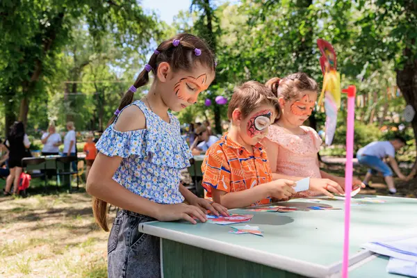 Önlerinde bir oyun tahtası olan üç çocuk bir masada oturuyorlar. Çocuklar birlikte oyun oynuyorlar ve ortam çok eğlenceli. 1 Haziran 2024 Balti Moldova.