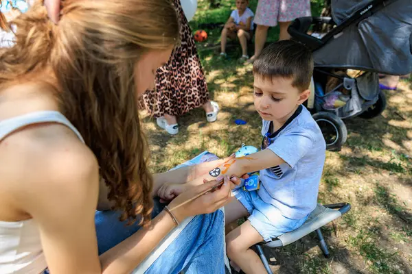 Kadın bir çocuğun elini boyuyor. Çocuk bir sandalyede oturuyor. Arka planda başkaları da var. 1 Haziran 2024 Balti Moldova.