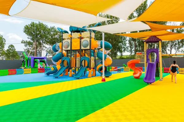 Büyük bir kaydırak ve oyun yapısı olan bir oyun alanı. Bir kadın oyun alanının yanından geçiyor. Oyun alanı renkli ve davetkar. 8 Haziran 2024 Balti Moldova