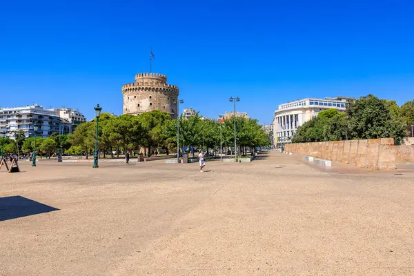 Arkasında büyük bir kule olan bir şehir meydanı. Gökyüzü açık ve mavi. Meydanın etrafında yürüyen birkaç kişi var. 8 Ağustos 2024 Selanik Yunanistan
