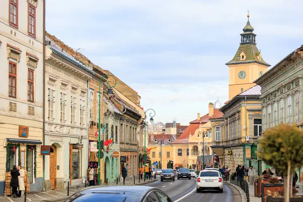 Arka planda saat kulesi olan işlek bir cadde. Sokak dükkanlarla dolu ve insanlar etrafta dolanıyor. 14 Aralık 2024 Brasov Romanya