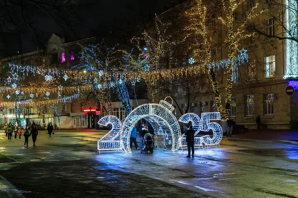 2025 dekorasyonlu ve geceleri gezen insanlarla dolu bir şehir caddesi. 27 Aralık 2024 Balti Moldova.