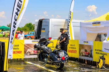 Bir motorcu, motosikletini dışarıdaki temizlik kabininde temizlemek için güçlü bir basınç makinası kullanır. Etkili araç temizleme ürünleri gösteriliyor. 2 Temmuz 2023 Liadoveni Moldova.