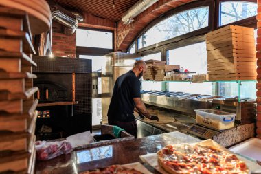 Erkek aşçı pizzacı mutfağında tuğla fırınıyla pizza hazırlıyor. 28 Aralık 2023 Balti Moldova.