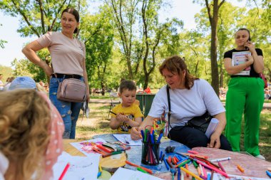 Bir grup insan üzerinde bir çocuk resmi olan bir masanın etrafında oturuyor. Sahne neşeli ve eğlenceli, çünkü bir grup insan etkinlikten zevk alıyor gibi görünüyor. 1 Haziran 2024 Balti Moldova.
