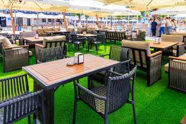 Yeşil çimlerde masaları ve sandalyeleri olan bir restoran. Masalar beyaz masa örtüleriyle kaplı ve üzerlerinde şemsiyeler var. Sandalyeler masaların etrafına dizildi. 8 Haziran 2024 Balti Moldova