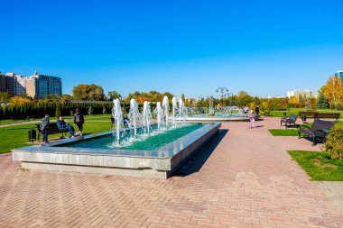 Arka planda birkaç kişinin oturduğu bir çeşme. Çeşme ağaçlar ve binalarla çevrilidir. 27 Ekim 2024 Chisinau Moldova