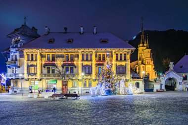 Önünde Noel ağacı olan büyük bir bina. Bina Noel ışıklarıyla aydınlanıyor. 13 Aralık 2024 Brasov Romanya