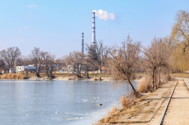 Soğuk bir kış gününde donmuş bir gölün yanındaki sanayi bacaları. 22 Şubat 2025 Balti Moldova.