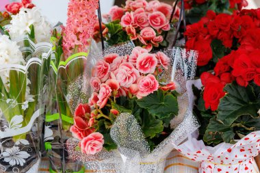 Bir buket pembe çiçek bir masanın üzerinde kırmızı bir buket çiçeğin yanında duruyor.