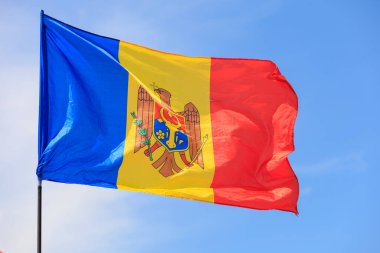Moldova Cumhuriyeti bayrağı. Moldova ulusal bayrağına yakın plan, belirgin kırmızı, sarı ve mavi renkleriyle, açık mavi gökyüzüne gururla el sallayarak, ulusal gurur ve birliği simgeliyor.