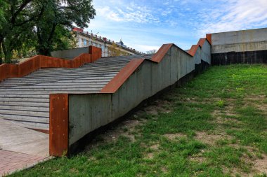 Beton duvarı ve merdiveni olan bir park. Duvar kahverengi ve merdivenler gri. Park boş ve gökyüzü mavi.
