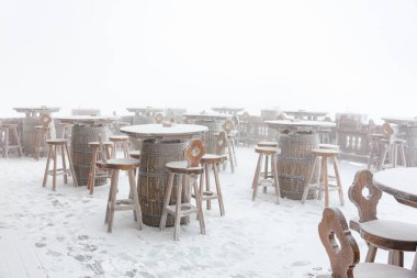Kışın harikalar diyarında ahşap masalar ve taburelerle karla kaplı bir bahçe..