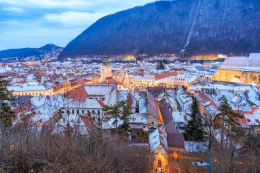 Geceleri binaların çatısında kar olan bir şehir. Şehir ışıklarla aydınlanıyor ve kar huzur dolu ve sakin bir atmosfer ekliyor.