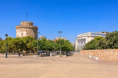 Arkasında büyük bir kule olan bir şehir meydanı. Gökyüzü açık ve mavi. Meydanın etrafında yürüyen birkaç kişi var. 8 Ağustos 2024 Selanik Yunanistan