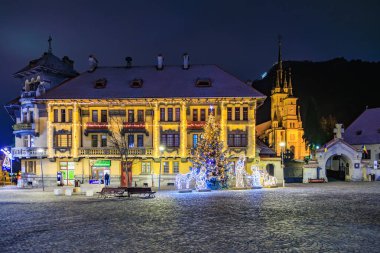 Önünde Noel ağacı olan büyük bir bina. Bina Noel ışıklarıyla aydınlanıyor. 13 Aralık 2024 Brasov Romanya
