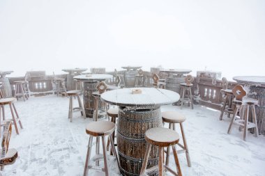 Kışın harikalar diyarında varil masaları olan karla kaplı açık bir kafe..