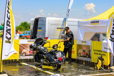 Bir motorcu, motosikletini dışarıdaki temizlik kabininde temizlemek için güçlü bir basınç makinası kullanır. Etkili araç temizleme ürünleri gösteriliyor. 2 Temmuz 2023 Liadoveni Moldova.