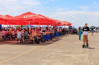 Ziyaretçiler parlak kırmızı şemsiyeler altında toplanarak, canlı bir açık havada gölgeli oturma ve günlük sohbetlerin keyfini çıkarıyorlar. 2 Temmuz 2023 Liadoveni Moldova.