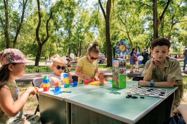 Bir grup çocuk parkta bloklarla ve masa oyunuyla oynuyorlar. Sahne eğlenceli ve eğlenceli, çünkü çocuklar birlikte dışarıda vakit geçiriyorlar. 1 Haziran 2024 Balti Moldova.