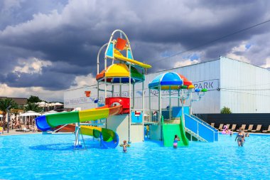 Büyük bir kaydırak ve gökkuşağı renkli bir kaydırak olan bir su parkı. Kaydırak şemsiyelerle çevrili ve insanlar suda oynuyorlar. 8 Haziran 2024 Balti Moldova