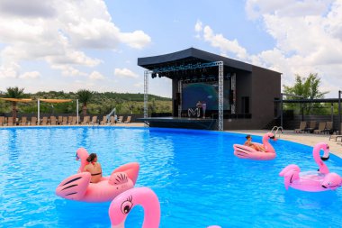 Bir grup insan havuzda pembe şişme sallarda yüzüyorlar. Sahne hareketli ve eğlenceli, insanlar suyun ve suyun tadını çıkarıyor. 8 Haziran 2024 Balti Moldova